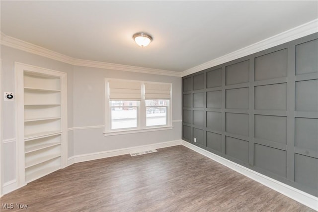 empty room featuring dark hardwood / wood-style flooring, built in features, and crown molding