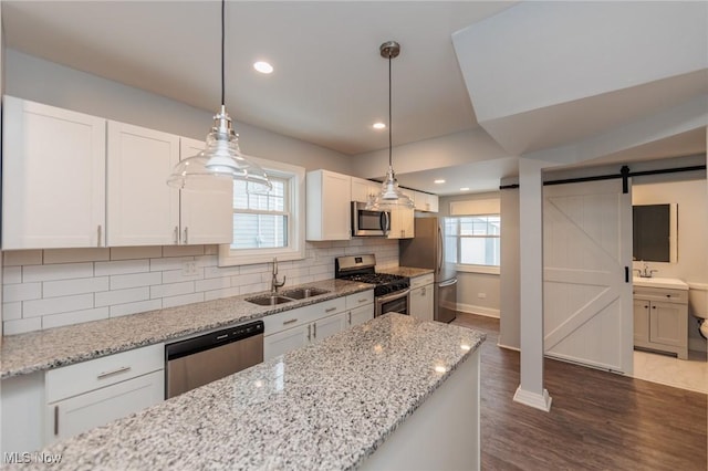 kitchen with pendant lighting, white cabinets, stainless steel appliances, sink, and a barn door