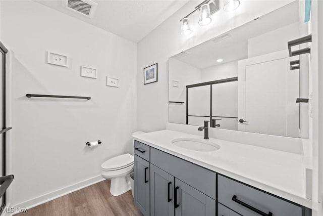 bathroom featuring wood-type flooring, toilet, a shower with shower door, and vanity