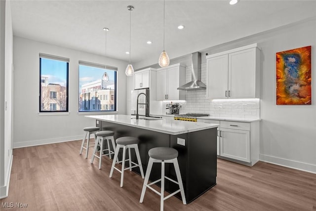 kitchen with white cabinetry, sink, a center island with sink, and wall chimney exhaust hood