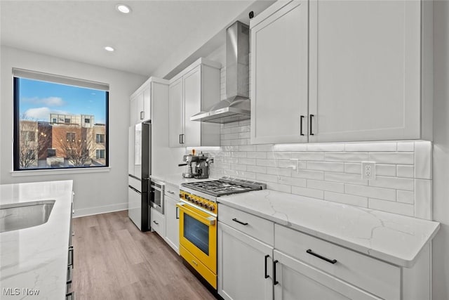 kitchen featuring white cabinetry, high end range, light stone countertops, and wall chimney range hood