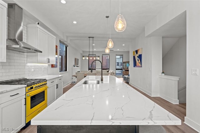 kitchen featuring pendant lighting, stainless steel stove, sink, wall chimney range hood, and a spacious island