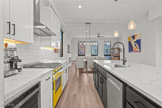 kitchen with white cabinetry, sink, hanging light fixtures, stainless steel appliances, and wall chimney exhaust hood