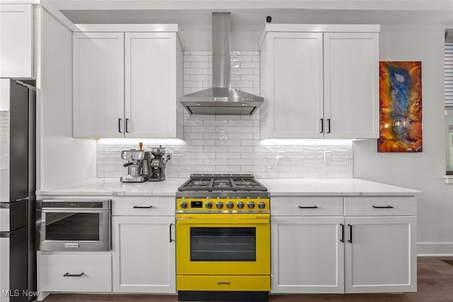 kitchen with wall chimney range hood, appliances with stainless steel finishes, light stone countertops, white cabinets, and decorative backsplash