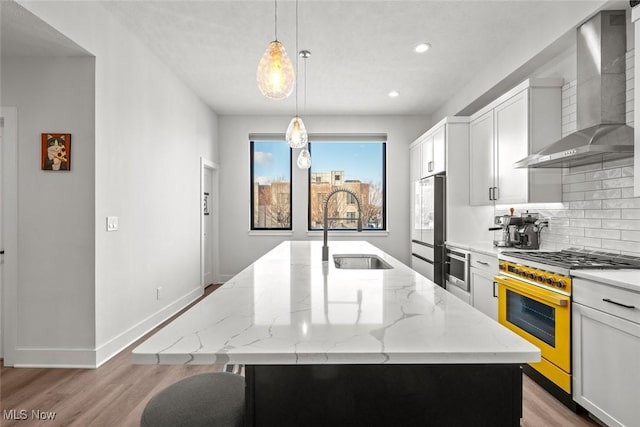 kitchen featuring pendant lighting, sink, stainless steel range, a center island with sink, and wall chimney exhaust hood