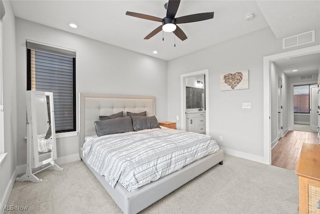 bedroom featuring light colored carpet, ceiling fan, and ensuite bath