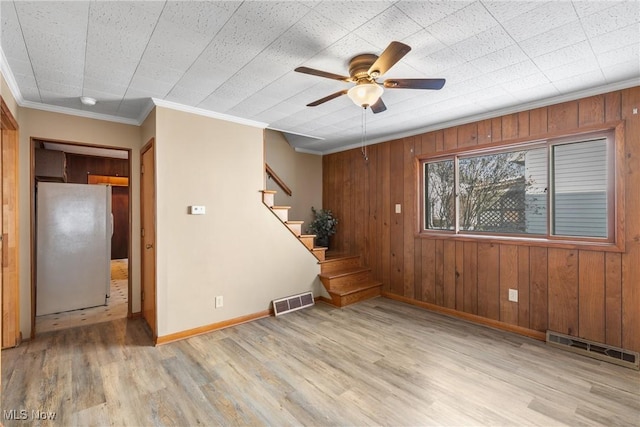 unfurnished room featuring wood walls, light hardwood / wood-style flooring, crown molding, and ceiling fan