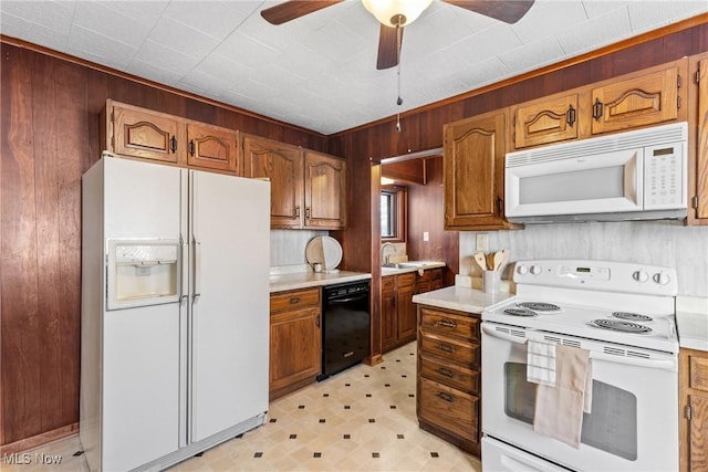 kitchen with ceiling fan, sink, white appliances, and wooden walls