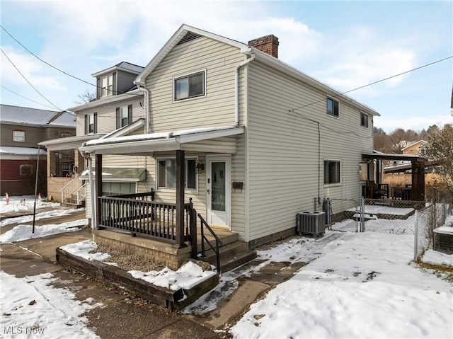 snow covered back of property featuring a porch and central AC