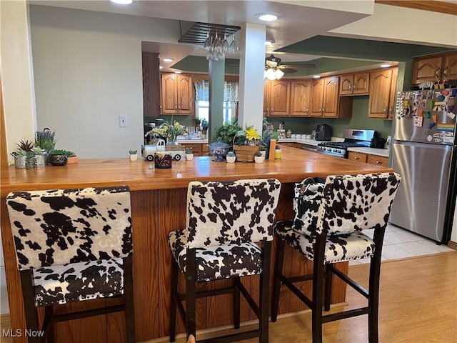 kitchen with a breakfast bar, appliances with stainless steel finishes, kitchen peninsula, and wooden counters