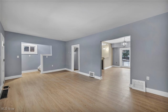 unfurnished living room with an inviting chandelier and light hardwood / wood-style flooring