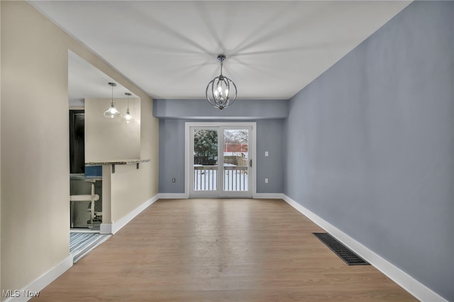 unfurnished room featuring a chandelier and light wood-type flooring