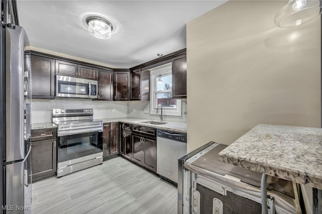 kitchen featuring light stone countertops, dark brown cabinetry, appliances with stainless steel finishes, tasteful backsplash, and sink