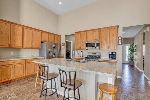 kitchen featuring a towering ceiling, a kitchen bar, stainless steel appliances, sink, and a center island with sink