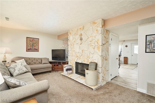 carpeted living room with a stone fireplace and a textured ceiling