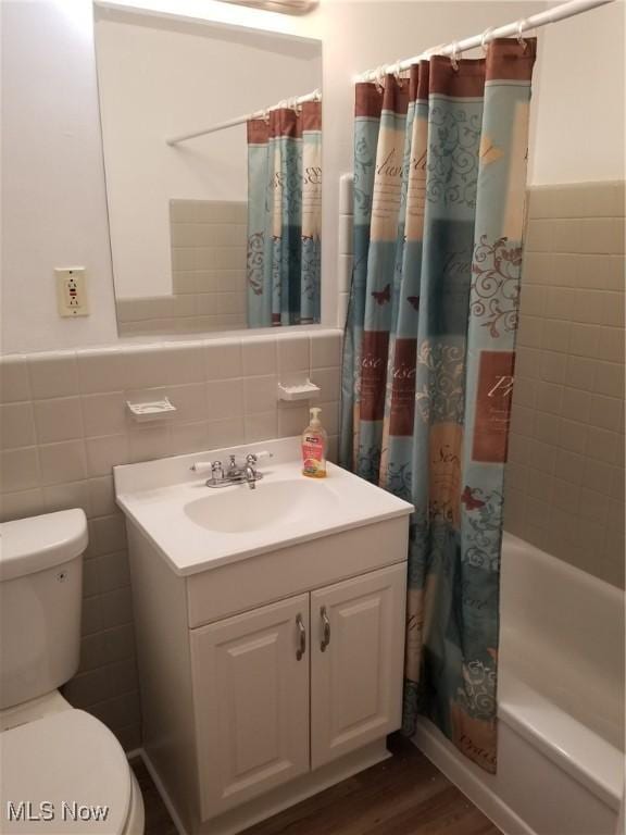 full bathroom with toilet, shower / bath combo with shower curtain, tile walls, wood-type flooring, and vanity