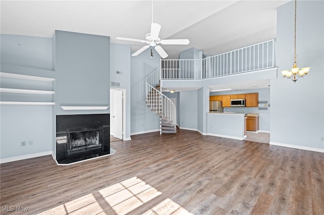 unfurnished living room with light wood-type flooring, a towering ceiling, and ceiling fan with notable chandelier