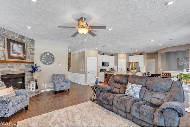 living room featuring ceiling fan, dark hardwood / wood-style floors, a stone fireplace, and a textured ceiling