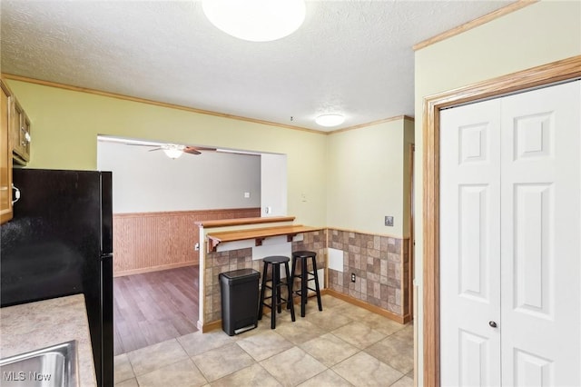 kitchen featuring a textured ceiling, light tile patterned floors, ornamental molding, and black refrigerator