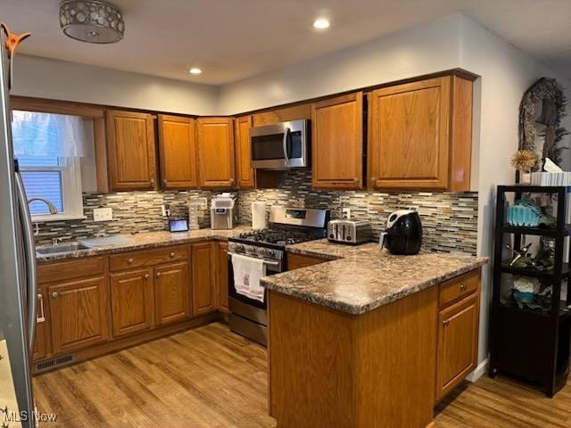 kitchen featuring dark stone countertops, light hardwood / wood-style floors, kitchen peninsula, decorative backsplash, and stainless steel appliances