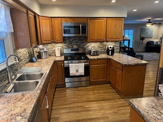 kitchen featuring light stone countertops, appliances with stainless steel finishes, wood-type flooring, decorative backsplash, and sink