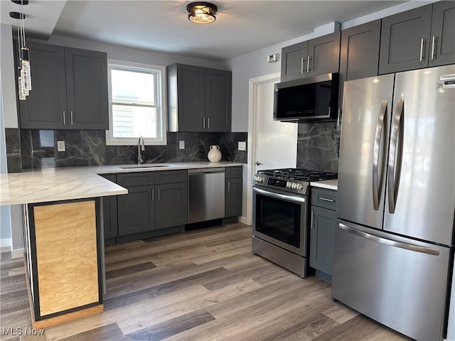 kitchen with sink, decorative light fixtures, appliances with stainless steel finishes, hardwood / wood-style floors, and decorative backsplash