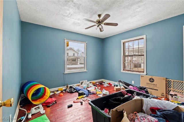 recreation room with ceiling fan, wood-type flooring, and a textured ceiling