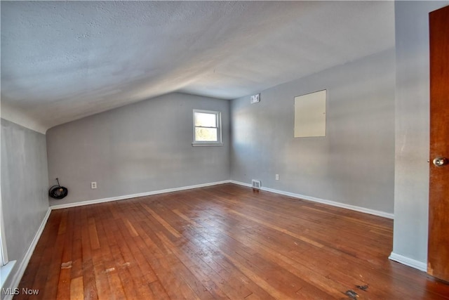 additional living space with lofted ceiling, wood-type flooring, and a textured ceiling