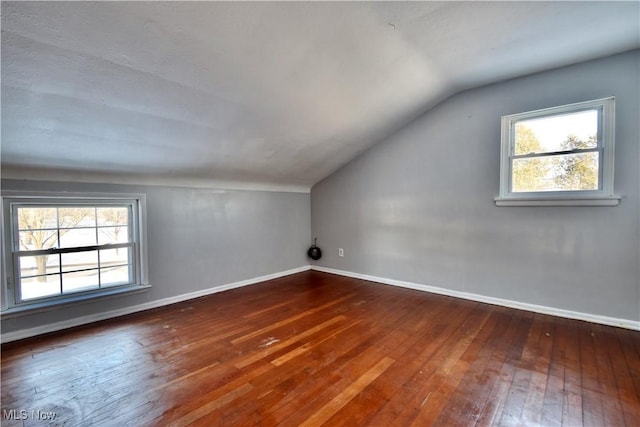 additional living space with a healthy amount of sunlight, vaulted ceiling, and dark hardwood / wood-style flooring