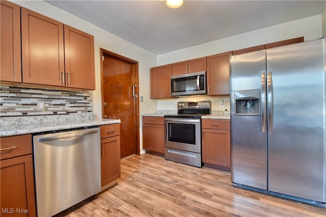 kitchen with light hardwood / wood-style floors, light stone countertops, decorative backsplash, and stainless steel appliances