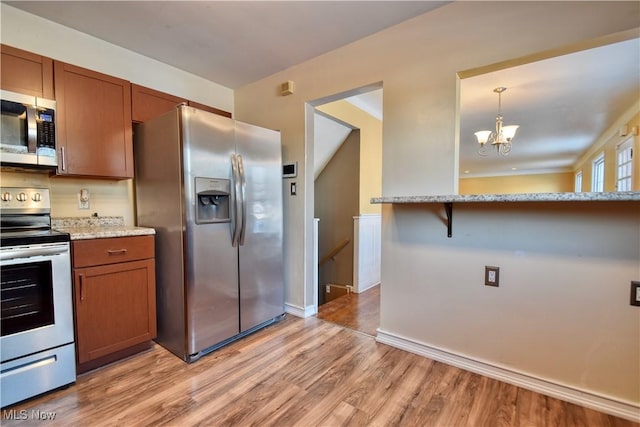 kitchen with light hardwood / wood-style floors, appliances with stainless steel finishes, decorative light fixtures, a notable chandelier, and light stone counters