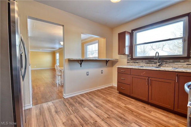 kitchen with backsplash, light hardwood / wood-style floors, sink, stainless steel fridge with ice dispenser, and light stone counters