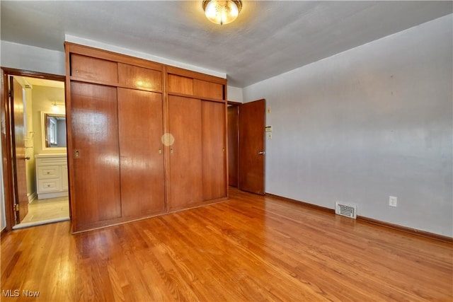 unfurnished bedroom featuring ensuite bathroom, a closet, and light hardwood / wood-style flooring