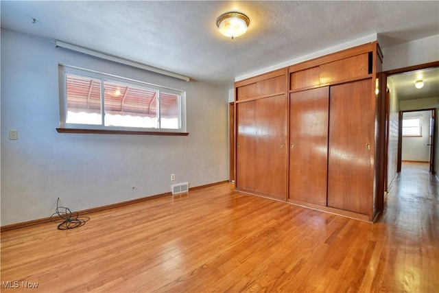 unfurnished bedroom featuring a textured ceiling, a closet, and light hardwood / wood-style flooring