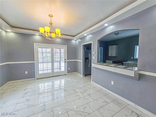 interior space with a raised ceiling, stainless steel fridge, an inviting chandelier, and hanging light fixtures