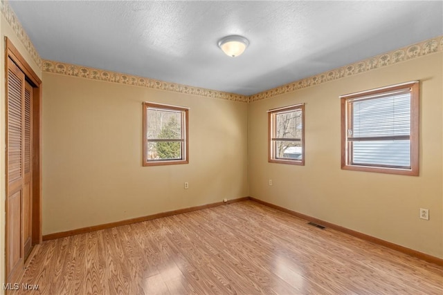 unfurnished bedroom featuring a closet, light hardwood / wood-style floors, and multiple windows