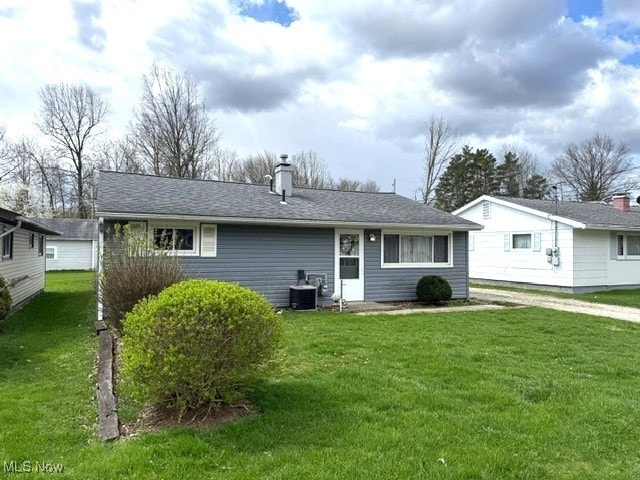 rear view of property featuring a shingled roof, a chimney, and a yard