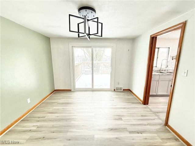 unfurnished dining area with sink, a notable chandelier, and light hardwood / wood-style flooring