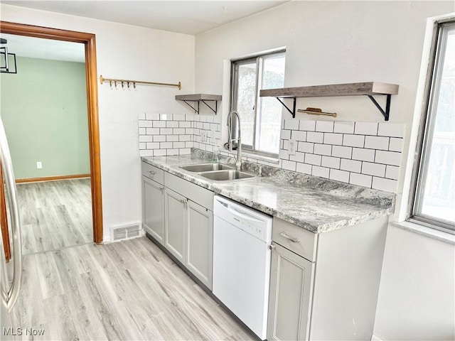 kitchen featuring sink, white cabinetry, light hardwood / wood-style flooring, white dishwasher, and decorative backsplash