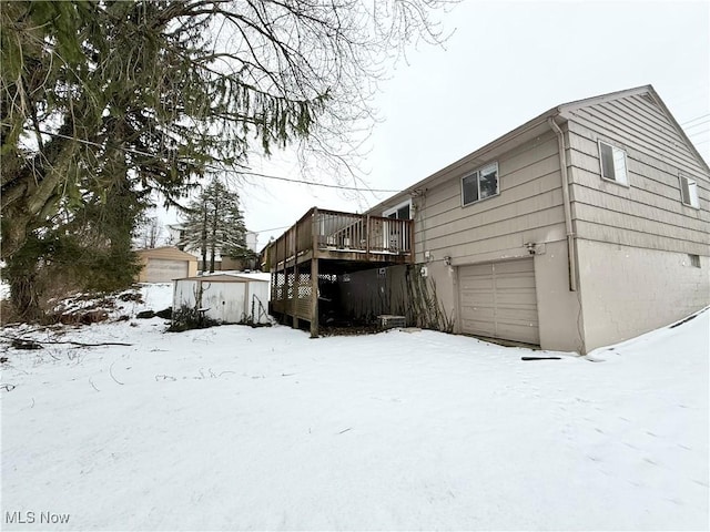 snow covered property with a garage and a wooden deck