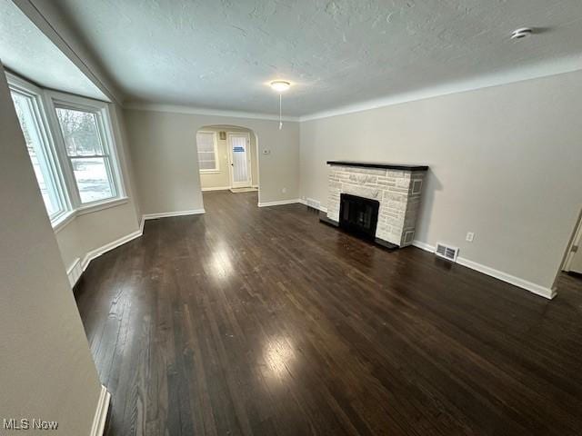 unfurnished living room with dark wood-type flooring, a stone fireplace, and a textured ceiling