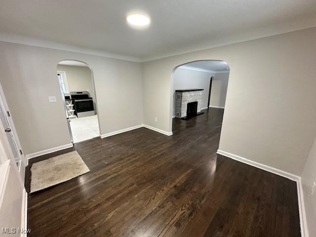 empty room with a brick fireplace and dark wood-type flooring