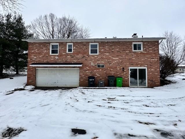 snow covered property with a garage and central AC