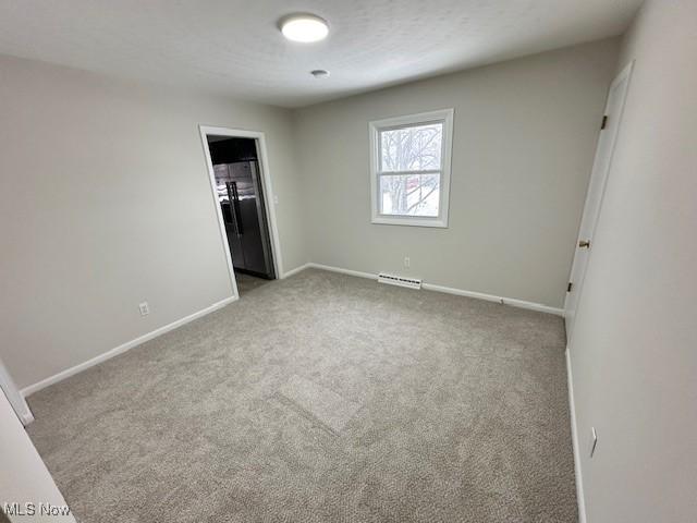 unfurnished bedroom featuring light carpet and a baseboard heating unit