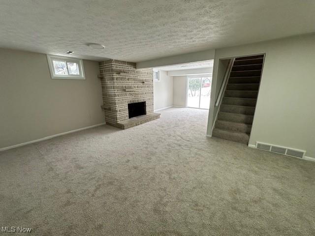 unfurnished living room with a textured ceiling, carpet flooring, and a stone fireplace