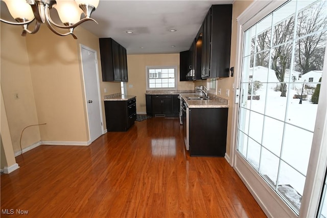 kitchen with hardwood / wood-style floors, dishwashing machine, sink, a chandelier, and light stone counters