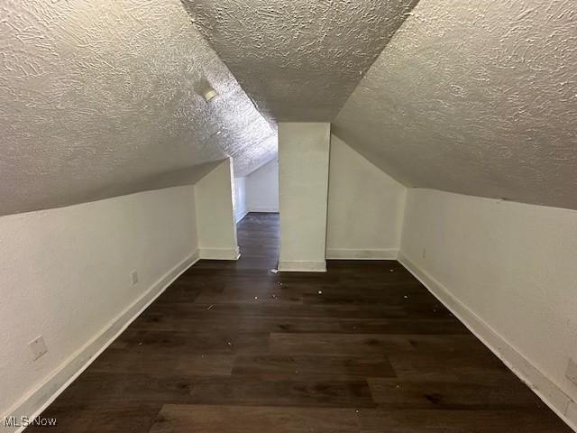 additional living space with vaulted ceiling, dark hardwood / wood-style flooring, and a textured ceiling