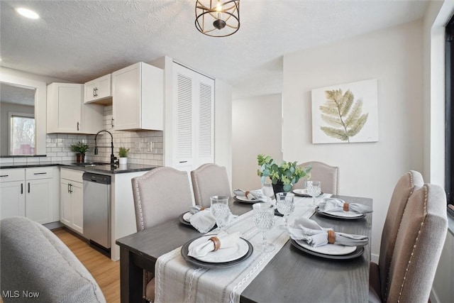 dining area featuring light wood-type flooring, a textured ceiling, a notable chandelier, and sink