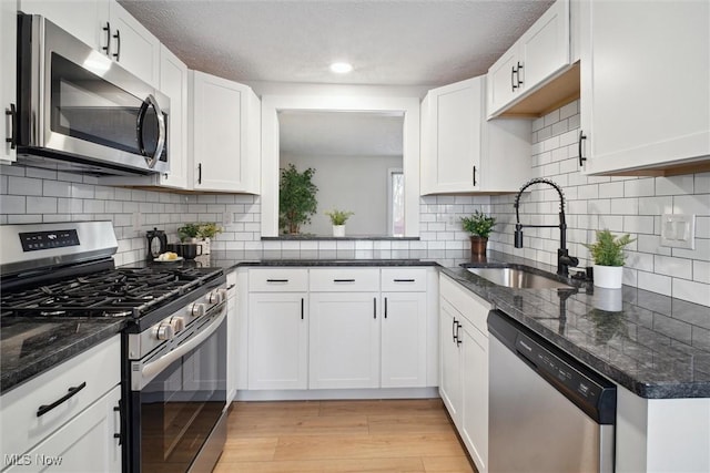 kitchen featuring stainless steel appliances, white cabinets, dark stone counters, and sink