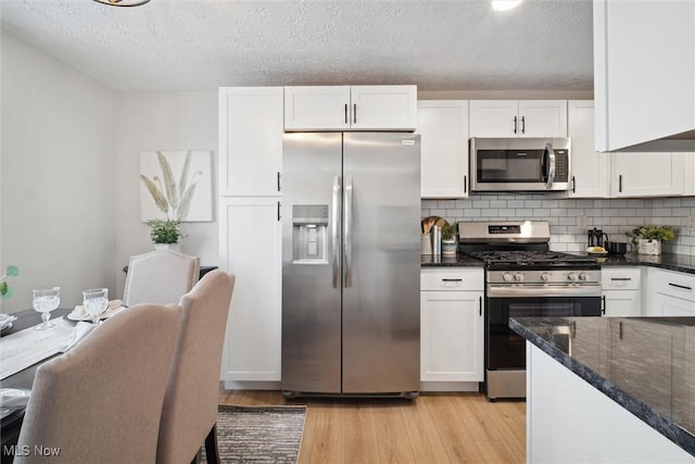 kitchen featuring appliances with stainless steel finishes, decorative backsplash, dark stone countertops, and white cabinets